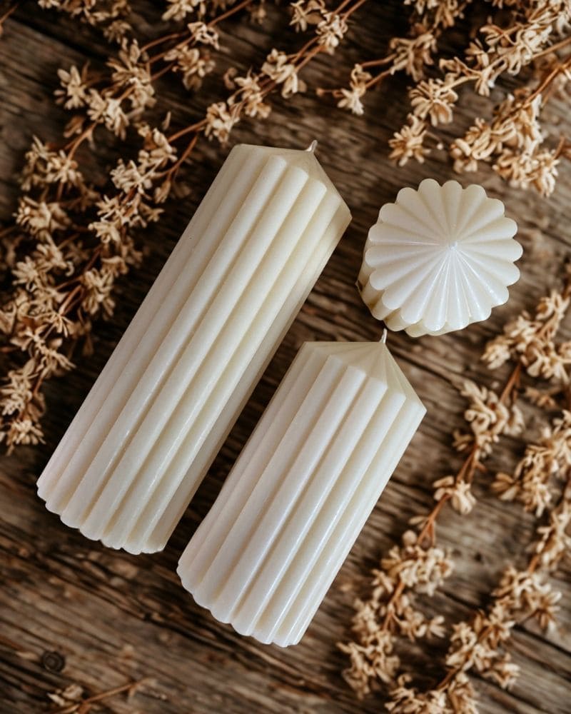 Candele artigianali bianche eleganti con striature verticali del set Orione su fondo rustico con decorazioni naturali.