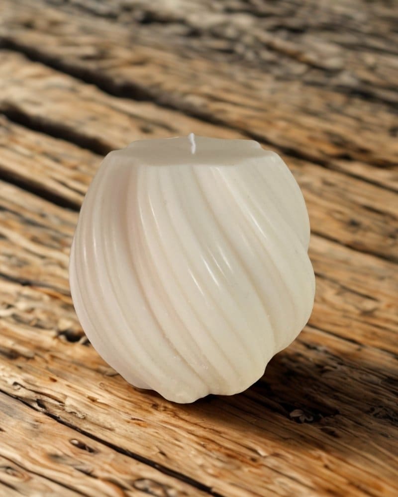 candela spenta d'arredo cosmika con striature oblique su un tavolo di legno rustico.