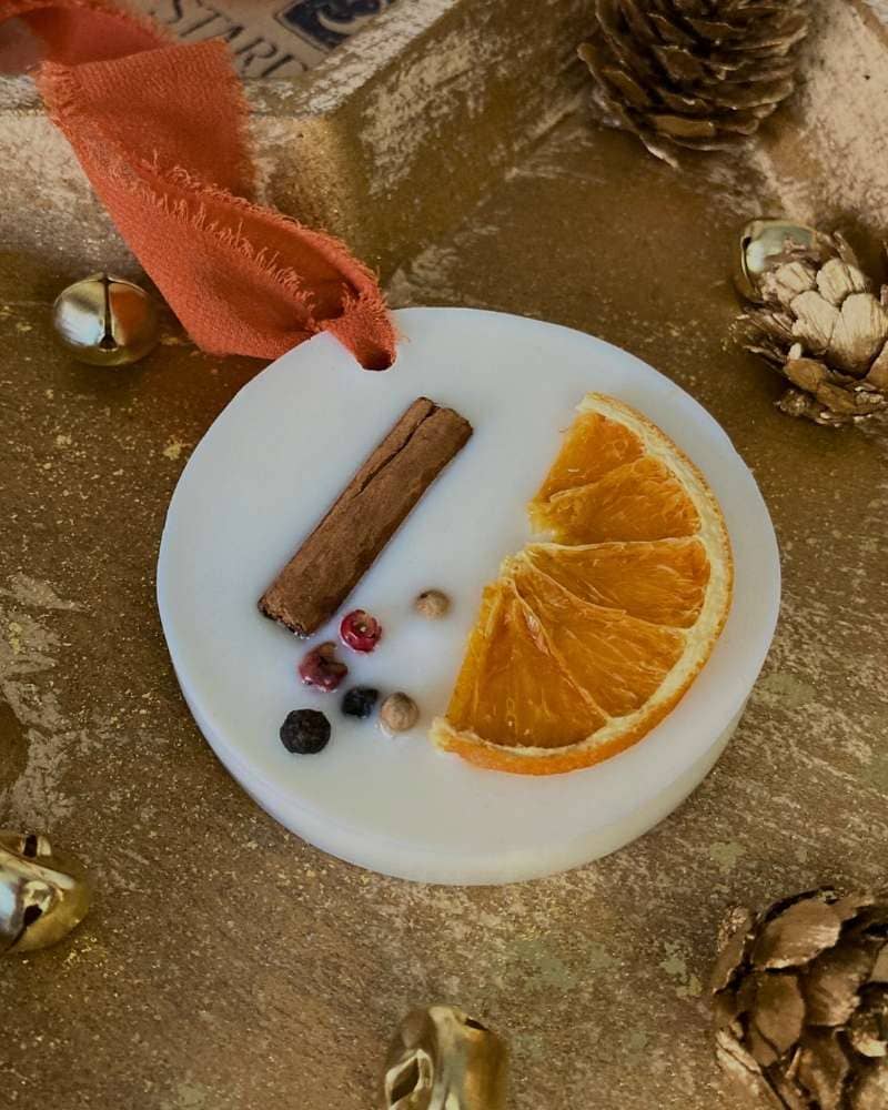 Cialda Gioisa un profumatore solido con nastro in chiffon arancione per appenderlo come decorazione natalizia. Realizzato in cera di soia e decorato con elementi Naturali: arancia essicata, cannella e spezie; nella sua confezione regalo Natalizia.
