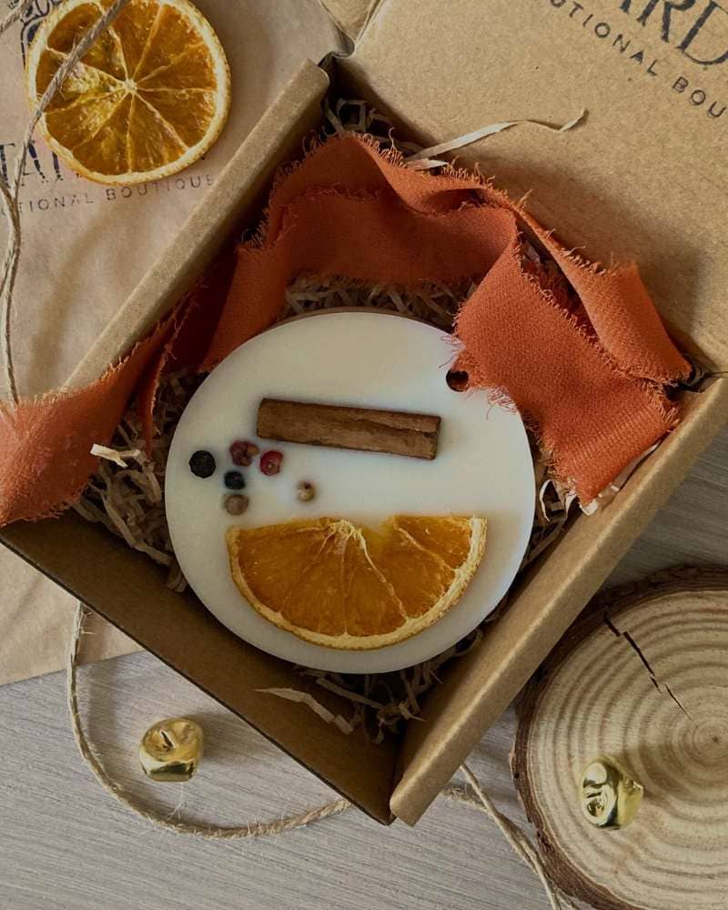 Cialda Gioisa un profumatore solido con nastro in chiffon arancione per appenderlo come decorazione natalizia. Realizzato in cera di soia e decorato con elementi Naturali: arancia essicata, cannella e spezie; nella sua confezione regalo Natalizia.