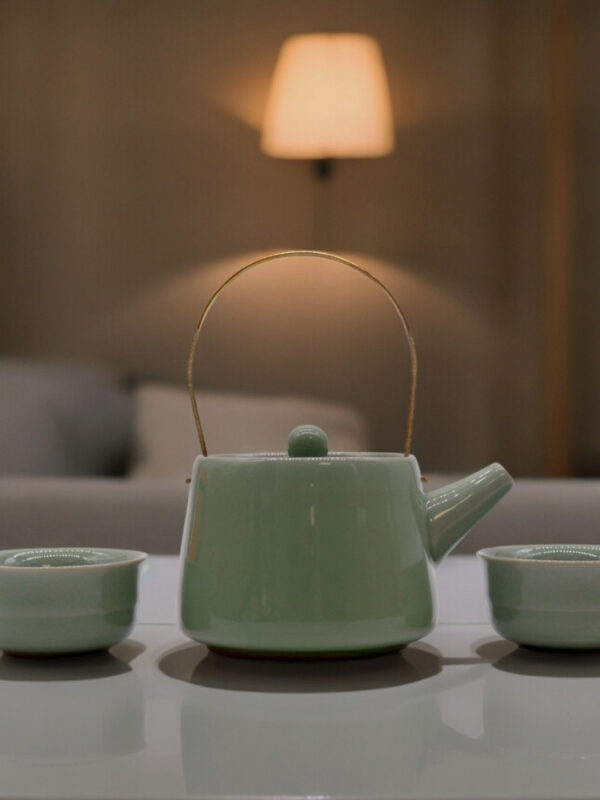 Teiera verde con due tazze in ceramica minimal su tavolo elegante
