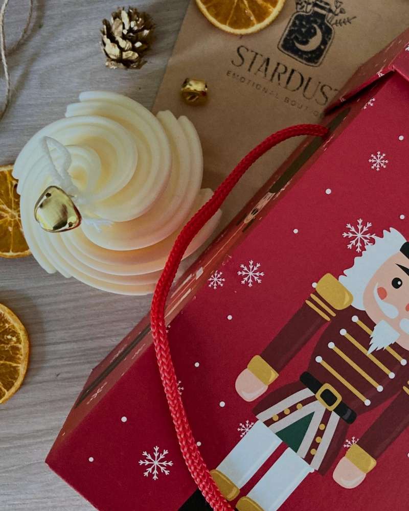 Candela Bianco natale a forma di albero di natale a spirale con campanellino dorato vista dall'alto vicino alla sua confezione regalo con illustrato uno schiaccianoci